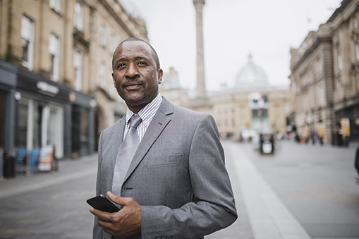 A man in a business suit holding a phone outside.