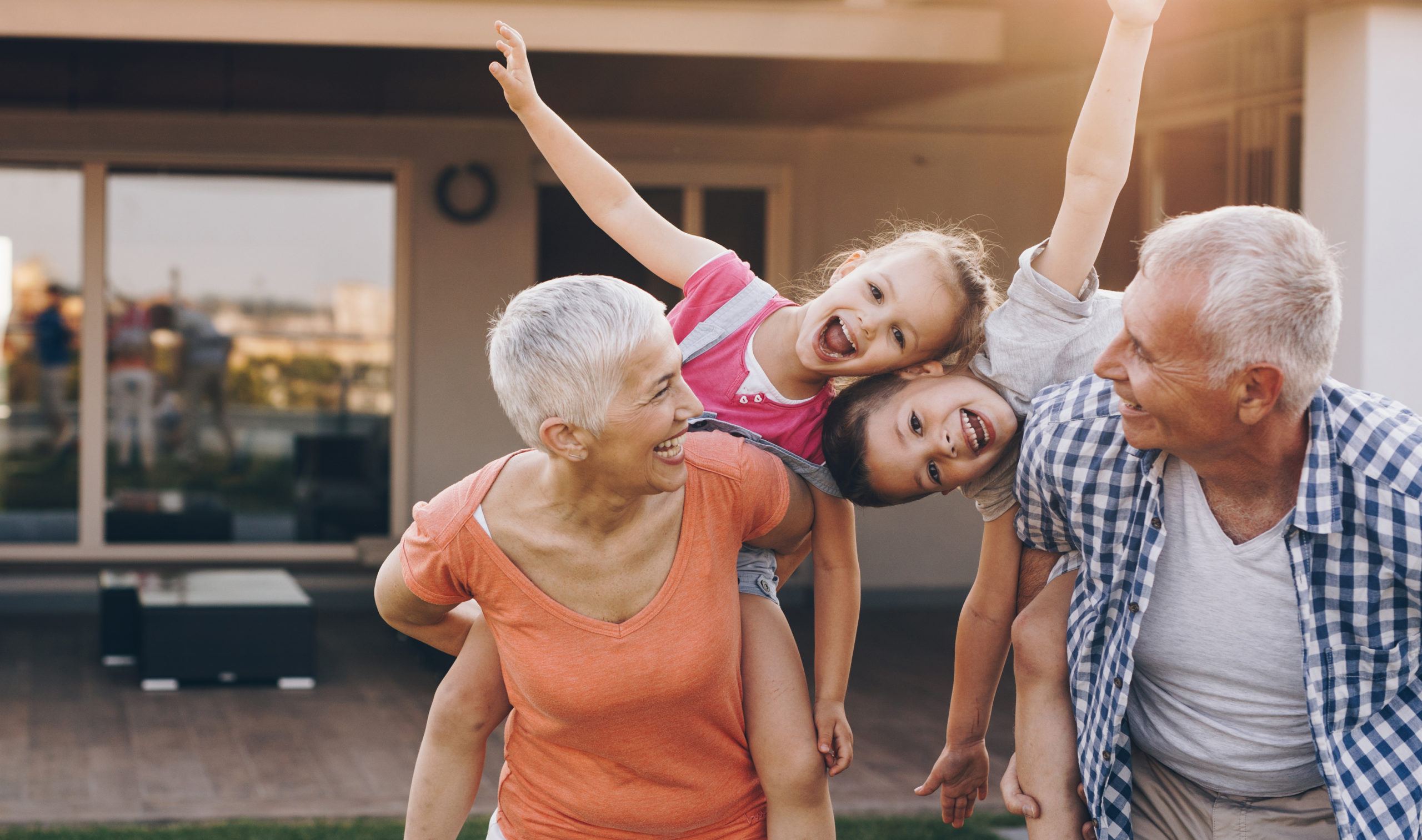 Carefree grandparents piggybacking their joyful grandkids in the front yard.