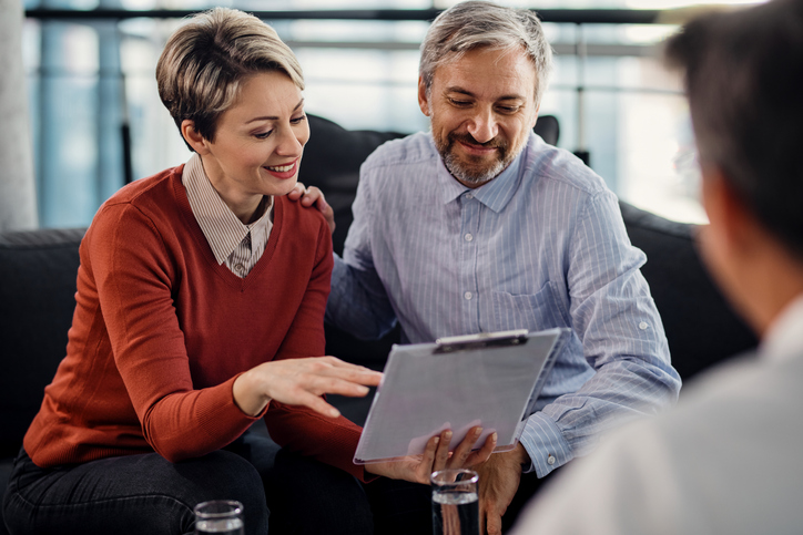 Happy couple analyzing documents while having a meeting with insurance agent in the office.
