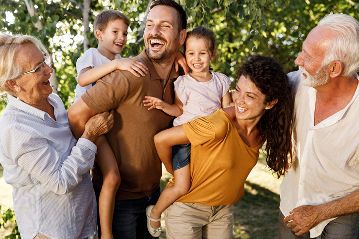 Cheerful multi-generation family having fun in nature. Parents are piggybacking their kids.