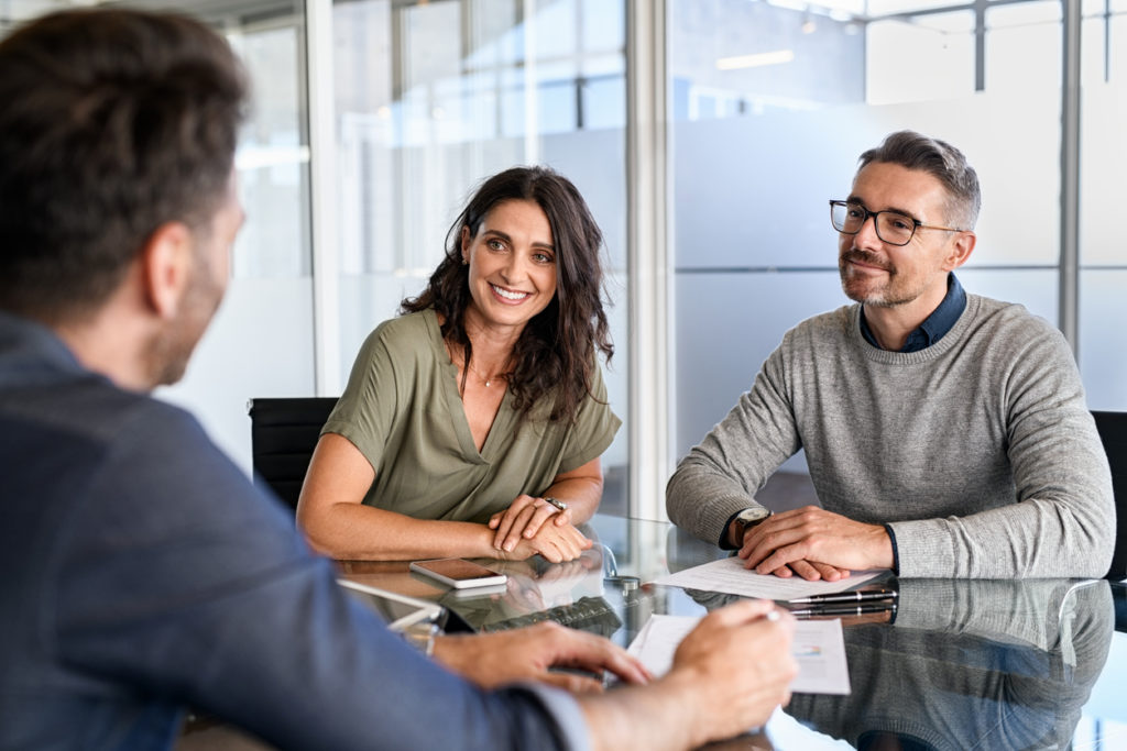 Smiling mature couple meeting with bank manager for investment. Beautiful mid adult woman with husband listening to businessman during meeting in conference room in modern office. Happy middle aged couple meeting loan advisor to buy a new home.