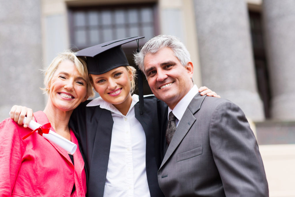 portrait of happy female university graduate and parents at ceremony.
