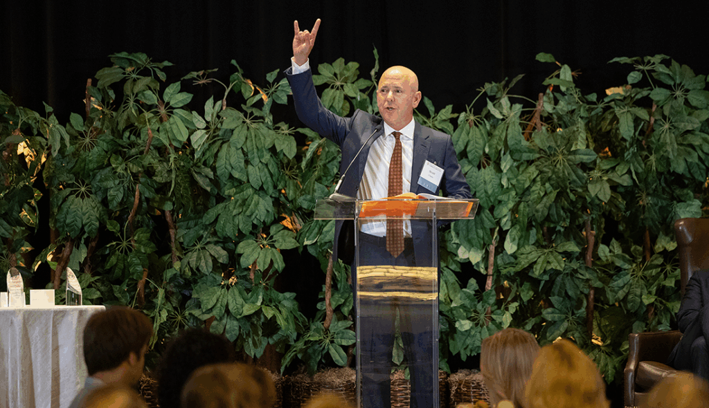 Businessman in a suit holding up the Hook 'Em Horns sign with his right hand.
