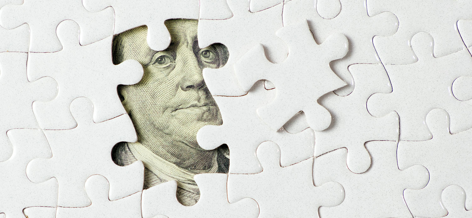US $100 banknote hidden under awhite jigsaw puzzle.